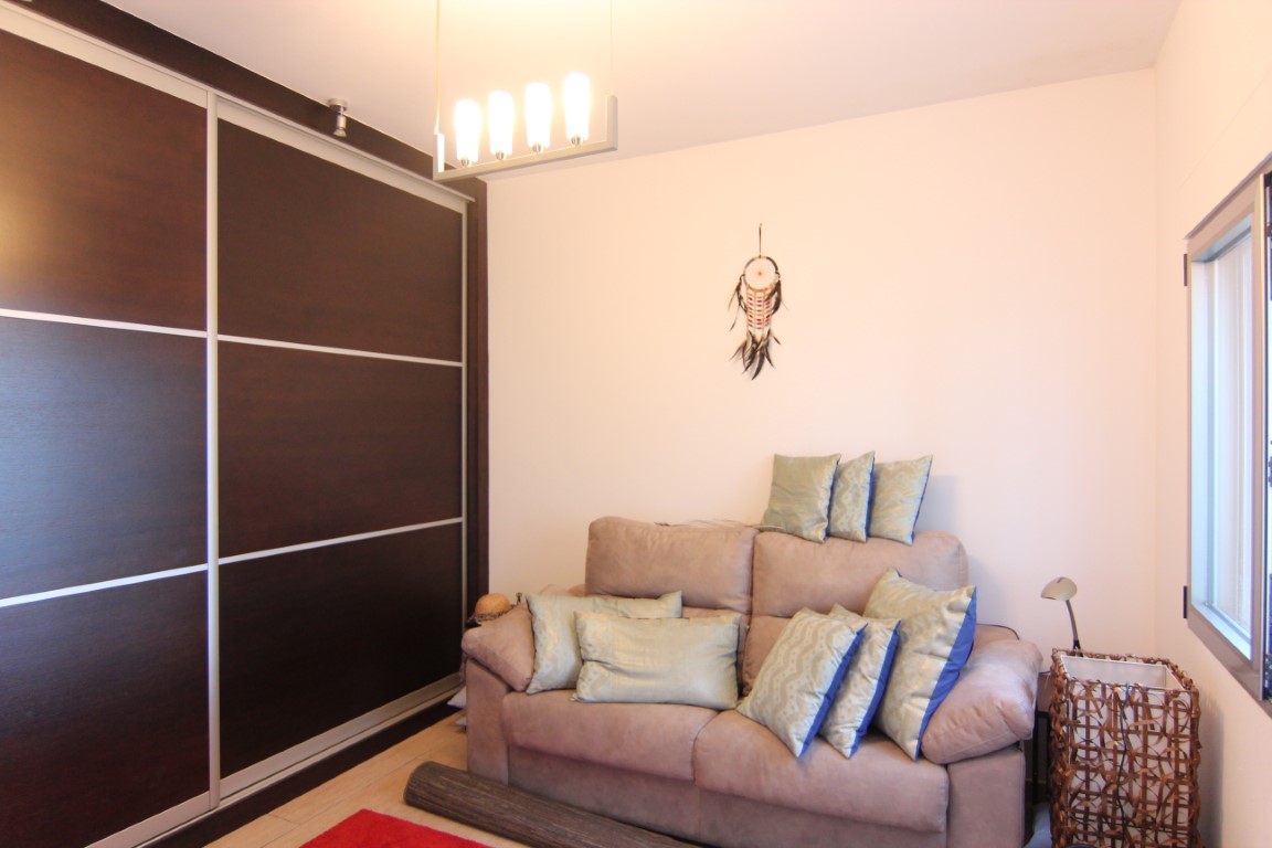 Bedroom featuring a large dark wood built-in wardrobe with sliding doors, a sofa with decorative cushions, and a modern four-bulb pendant light.