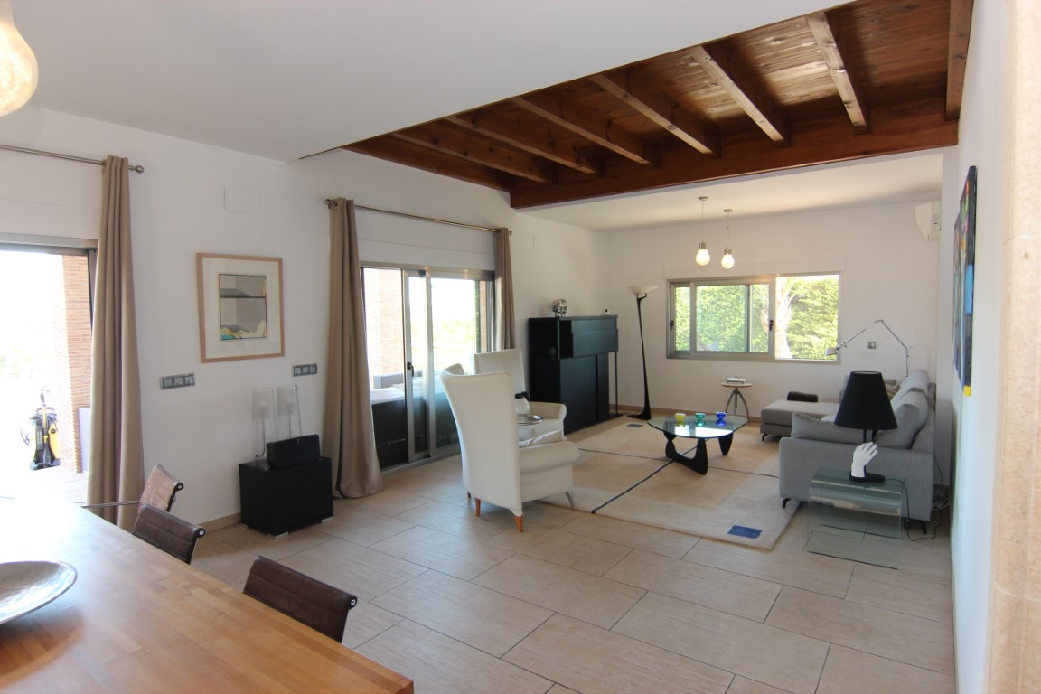 Bright living area featuring exposed wooden ceiling beams, light tile flooring, and large sliding glass doors leading to the terrace.