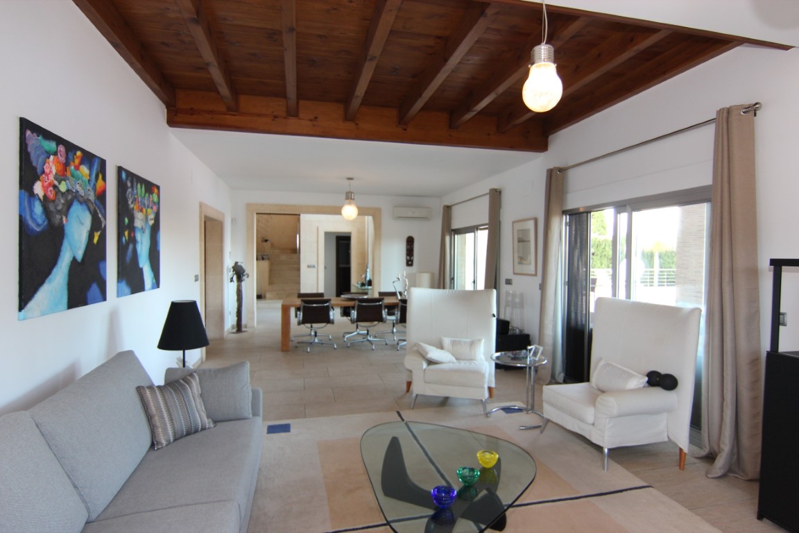 Bright living room featuring exposed wooden ceiling beams, large sliding glass doors to the terrace, and an open-plan layout connecting to the dining area.