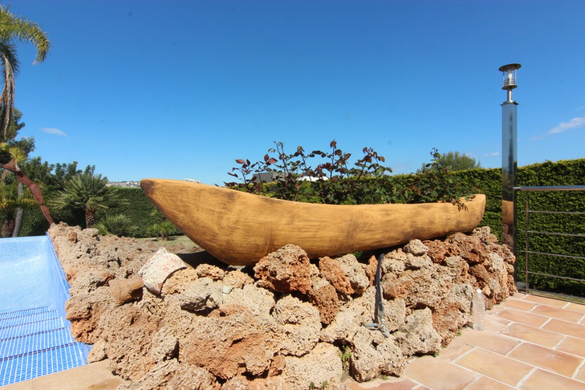 Decorative boat-shaped planter resting on a natural rock wall by the pool, featuring terracotta tiling and modern outdoor lighting.