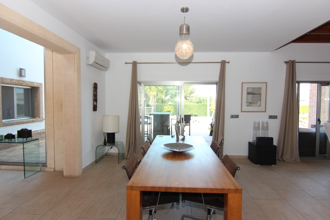 Dining space featuring a solid wood table and ceramic tiling, with direct access to the outdoor terrace through large sliding glass doors.