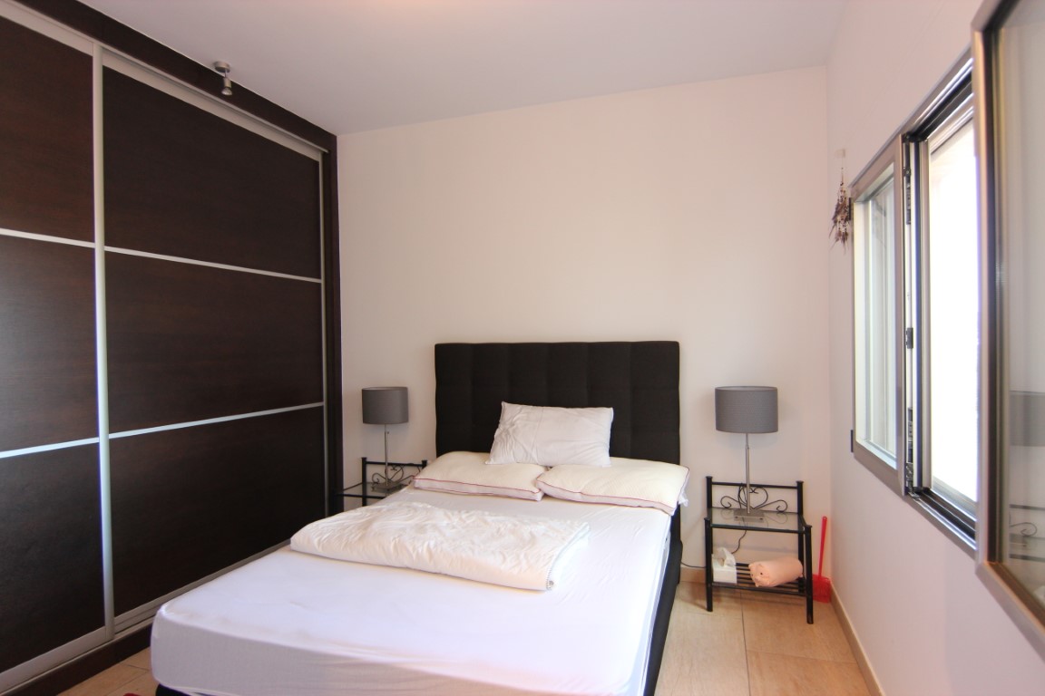 Double bedroom featuring a large dark wood sliding-door wardrobe, minimalist glass bedside tables, and natural light from the side window.