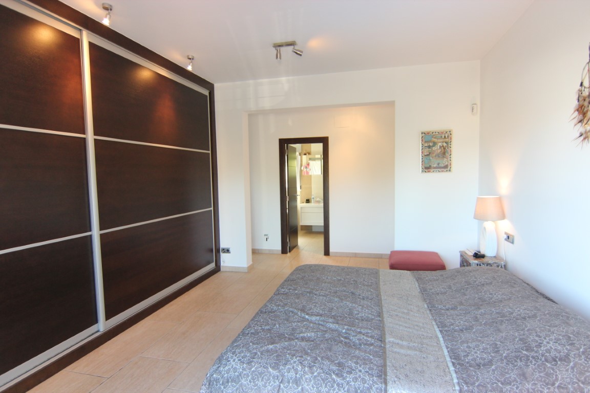 Double bedroom featuring a large dark wood sliding wardrobe and tiled flooring. The open doorway reveals a modern en-suite bathroom with a white vanity unit.