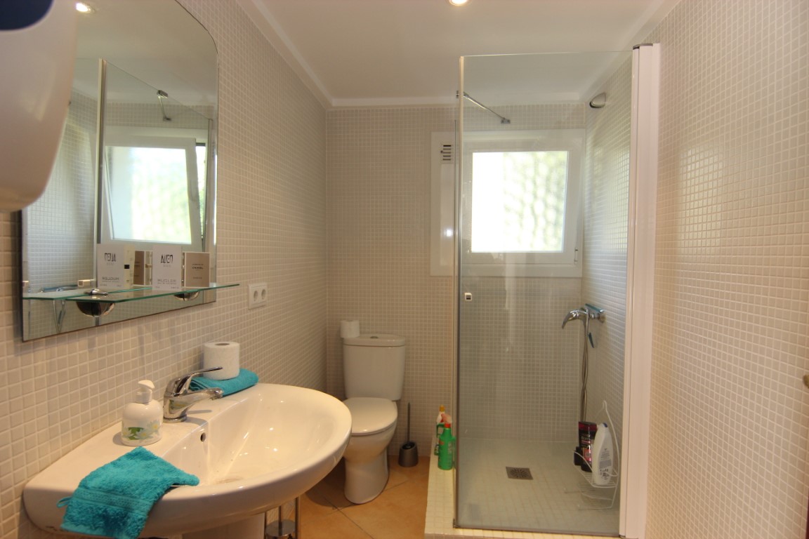 Functional bathroom featuring beige mosaic wall tiles, a walk-in shower with a glass screen, and a white ceramic sink. A small window provides natural light.