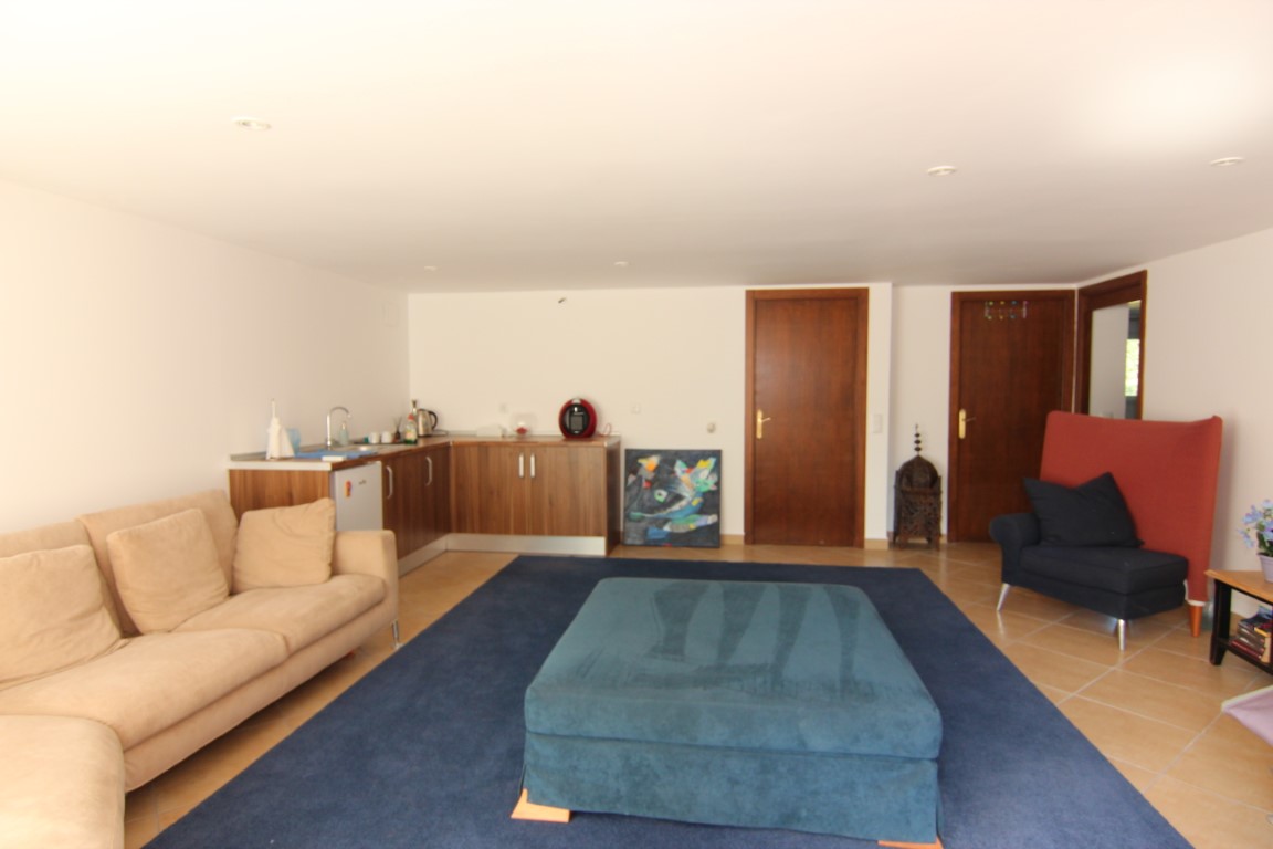 Guest apartment living area featuring a functional kitchenette, recessed lighting, ceramic tile flooring, and a spacious lounge with integrated blue textiles.