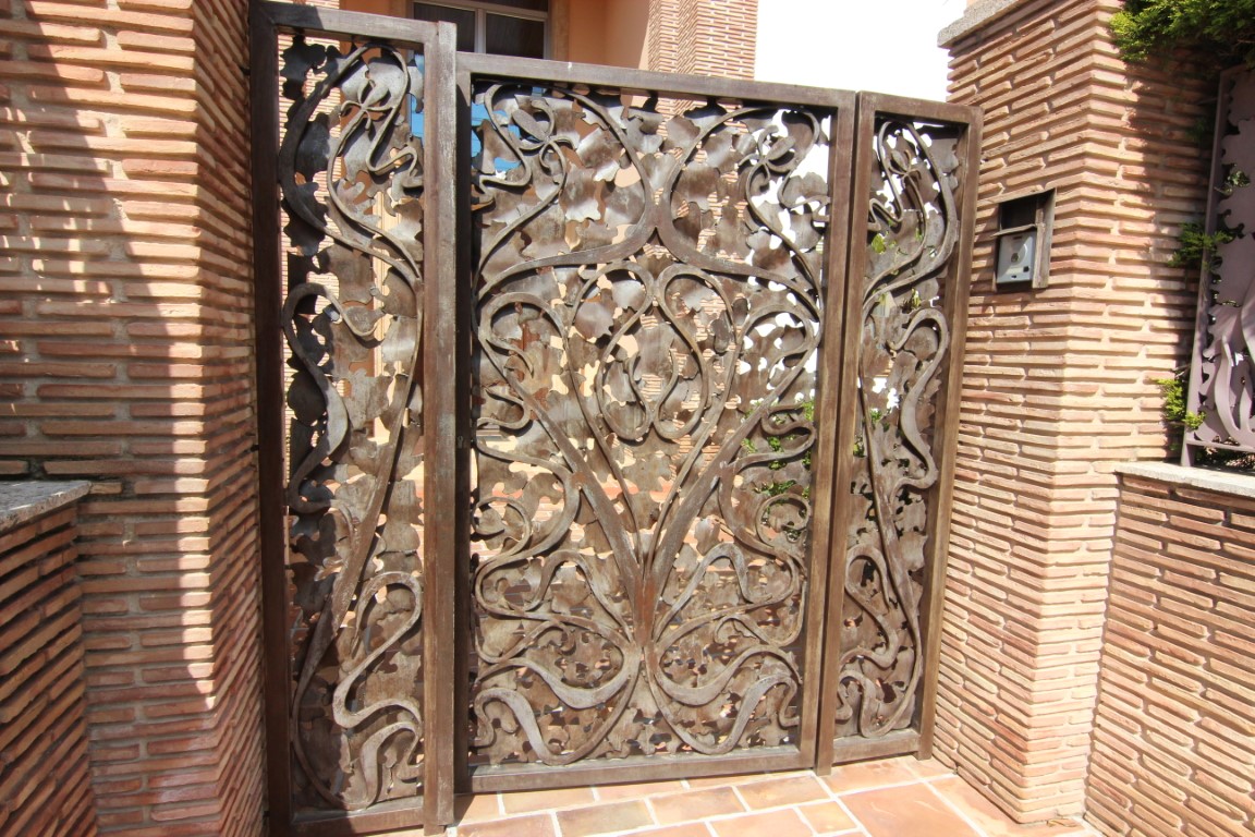 Handcrafted metal entrance gate featuring an organic leaf-inspired design, set between textured brick pillars.