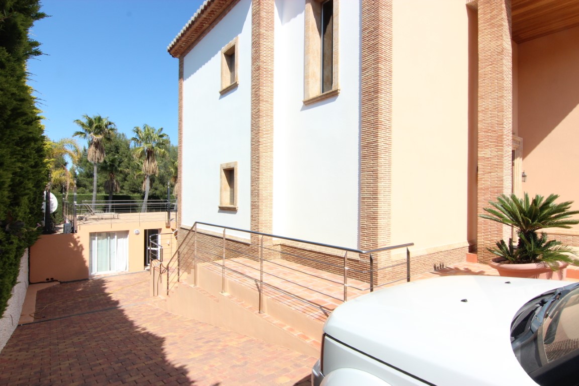 Main entrance featuring an access ramp with stainless steel railings. The facade combines white plaster with decorative brick columns and natural stone window surrounds.