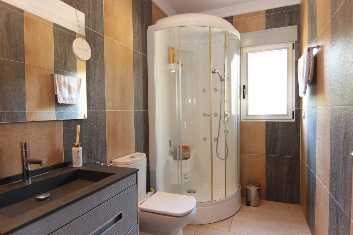 Modern bathroom featuring a curved glass shower enclosure, earth-toned vertical wall tiles, and a sleek dark vanity with integrated basin.