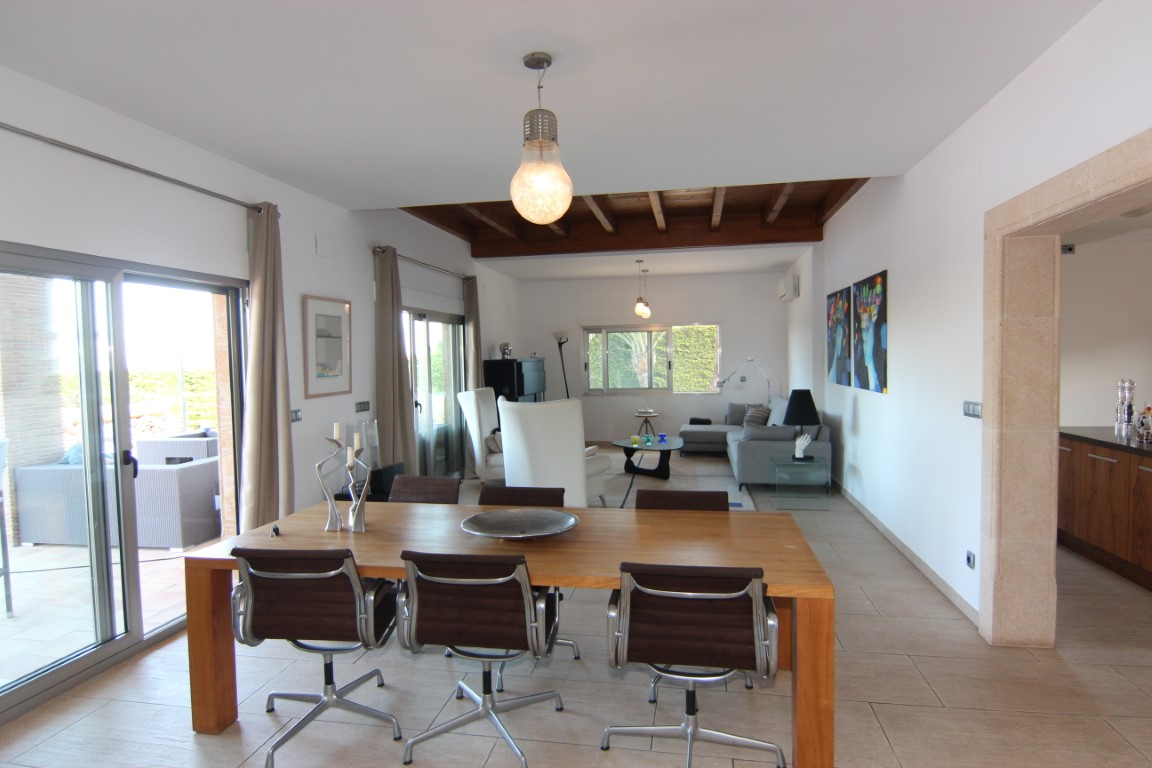 Open-plan living and dining area featuring exposed wooden beams, a solid wood table, and large sliding glass doors opening onto the outdoor terrace.