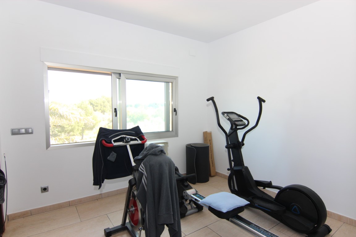 Private home gym featuring fitness equipment and tiled flooring, illuminated by natural light from a large sliding window with garden views.