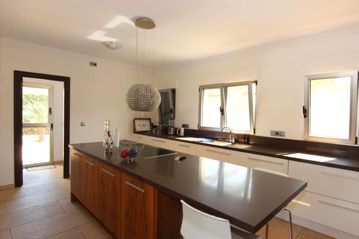 Spacious kitchen featuring a wooden central island with dark countertops and a crystal pendant. Includes integrated appliances and direct access to the garden.