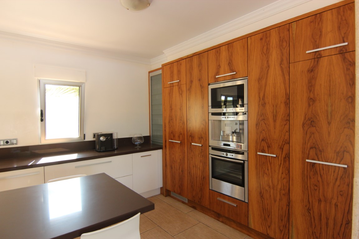 Spacious kitchen featuring natural wood cabinetry, integrated stainless steel appliances, and dark countertops paired with white base units.