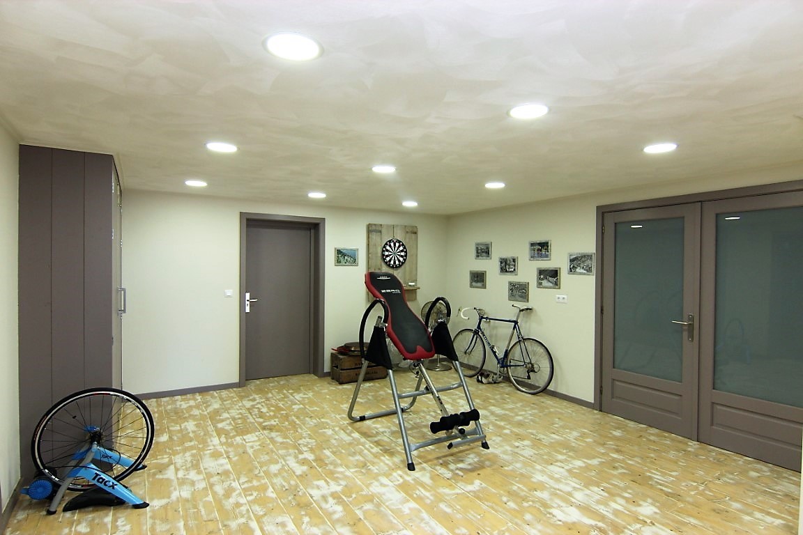 Basement fitness room featuring light-toned wooden flooring, recessed ceiling lighting, and ample space for sports equipment and exercise machines.