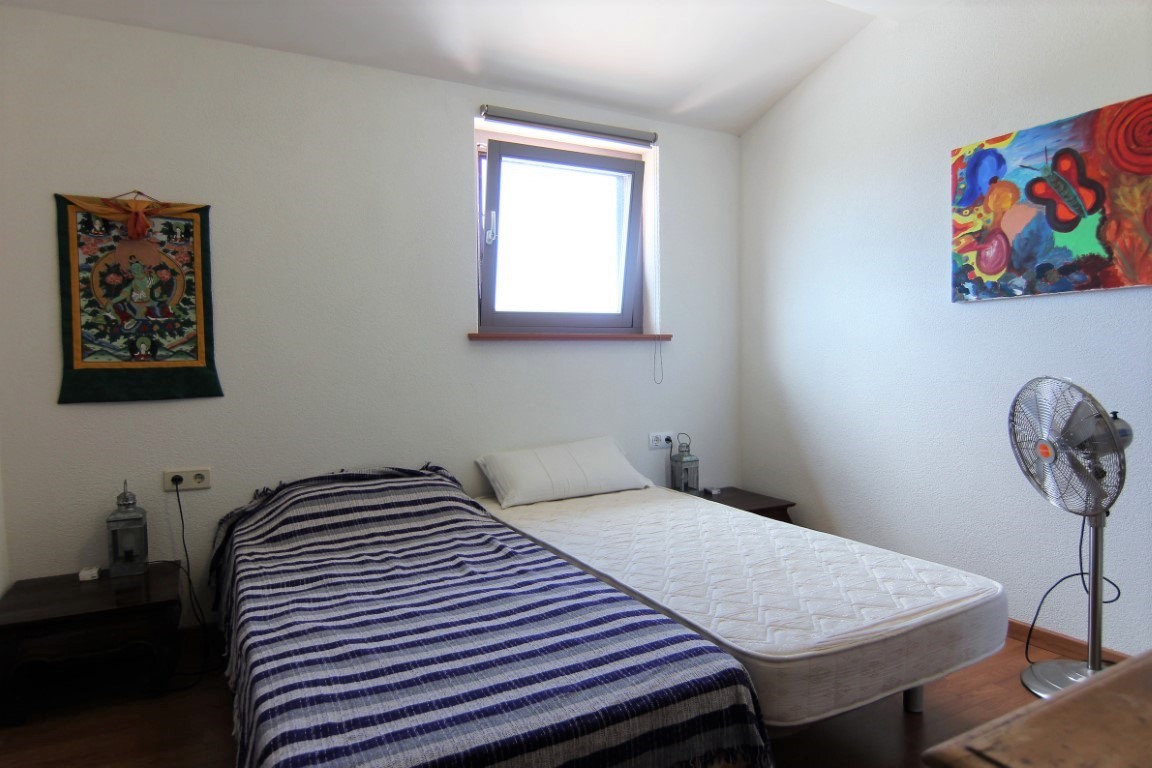 Bright bedroom featuring two single beds, wooden flooring, and white walls decorated with vibrant artwork, receiving natural light from a central window.