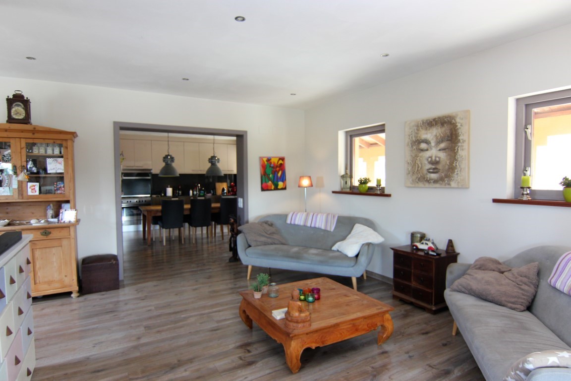 Bright living area with wood-effect flooring and rustic furniture, featuring an open-plan transition to a modern kitchen and dining space.