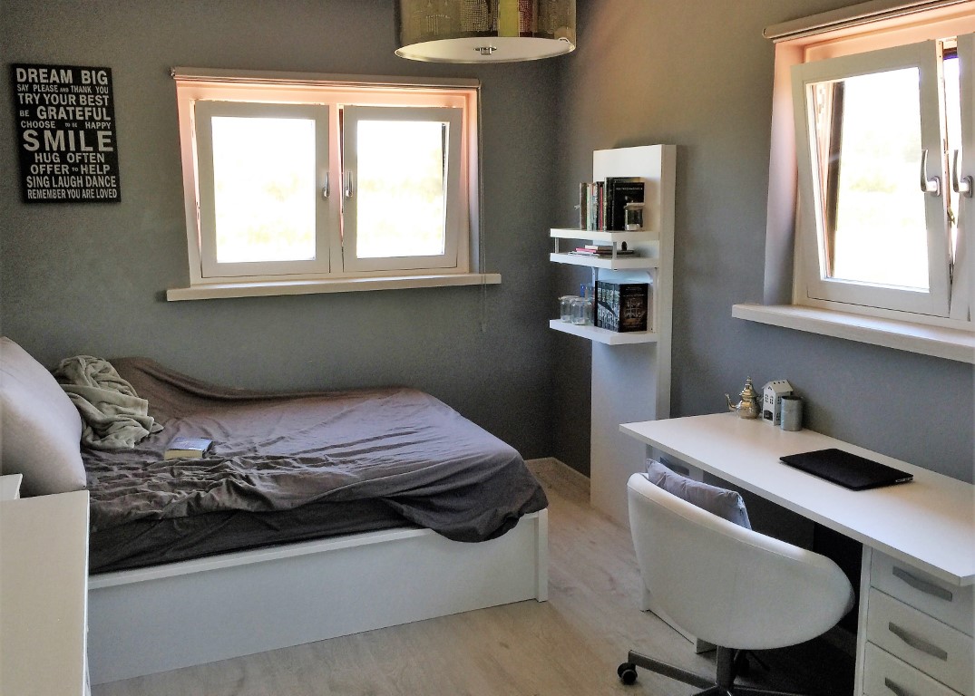Double bedroom featuring a dedicated workspace with a white desk, grey walls, and light wood flooring. Two windows ensure plenty of natural light.