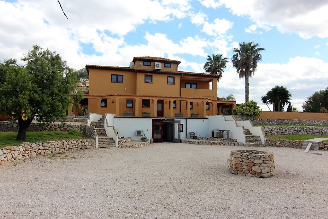 Exterior perspective of the three-story property showcasing the ochre facade, stone retaining walls, and a gravel courtyard with a traditional stone well.