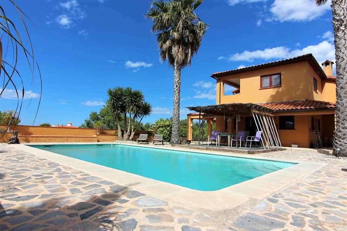 Exterior view featuring a rectangular swimming pool, natural stone terrace, and a rustic wooden pergola seating area set against the terracotta facade.