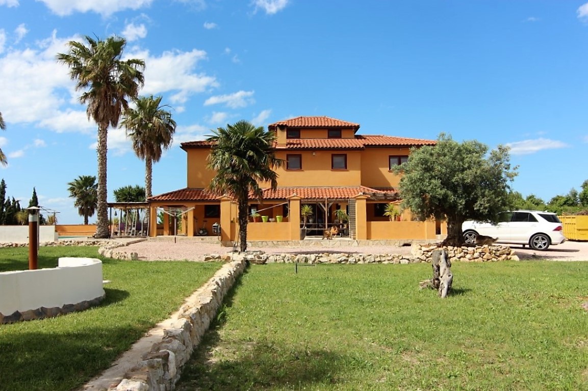 Exterior view of the three-story finca featuring an ochre facade, terracotta roofs, and expansive lawns bordered by natural stone walls.
