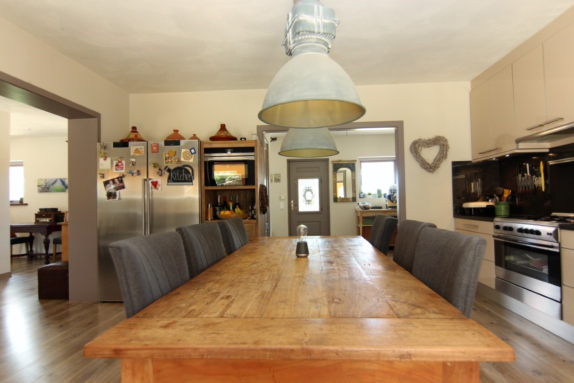 Kitchen and dining area featuring a large rustic wooden table, industrial pendant lighting, and modern stainless steel appliances integrated into cream cabinetry.