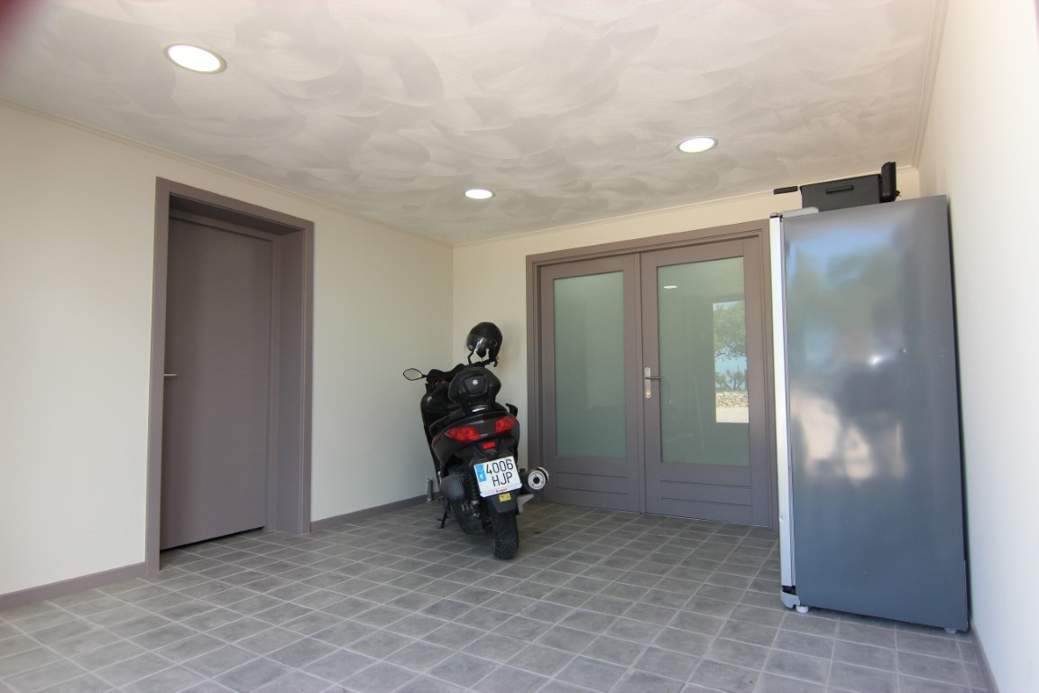 Storage or garage area featuring grey tiled flooring, recessed ceiling spotlights, and double glass doors providing external access.