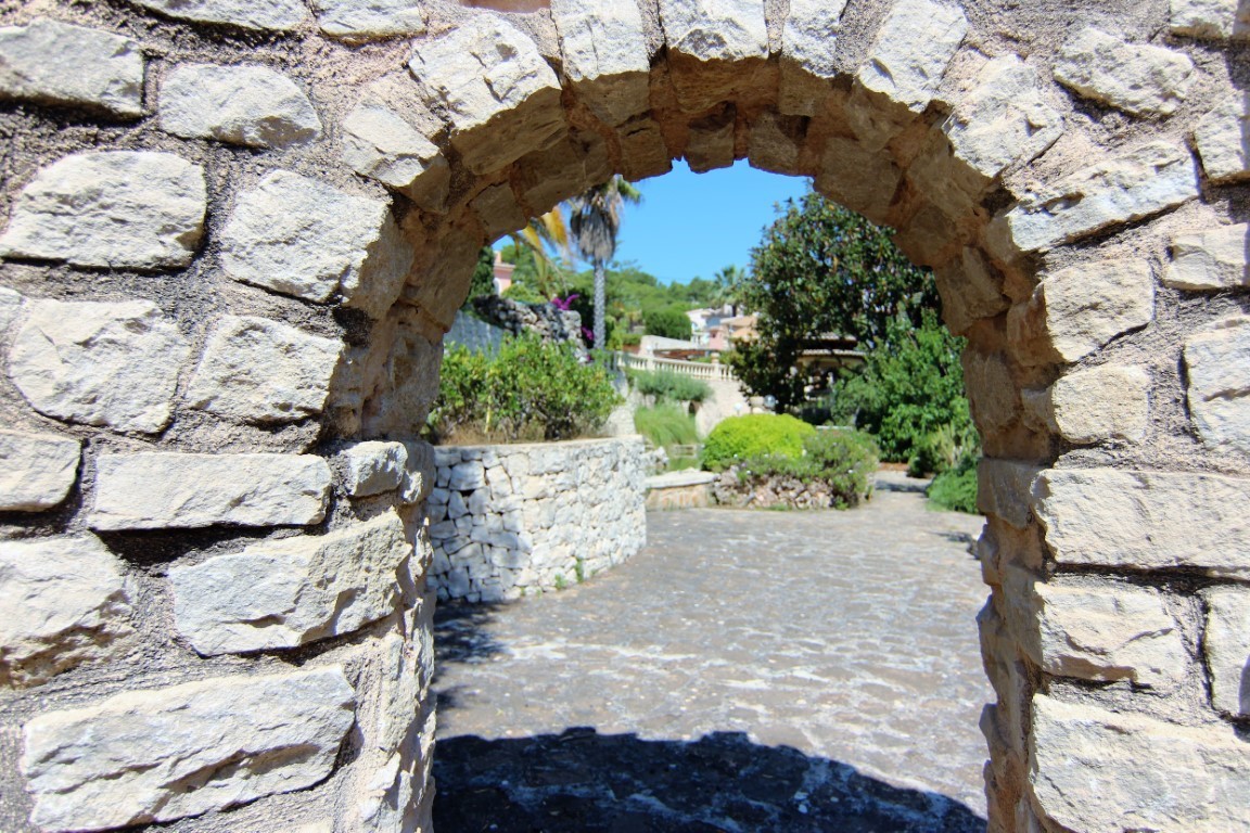 A natural stone archway frames the entrance to the Mediterranean gardens, featuring paved pathways and dry-stone retaining walls.