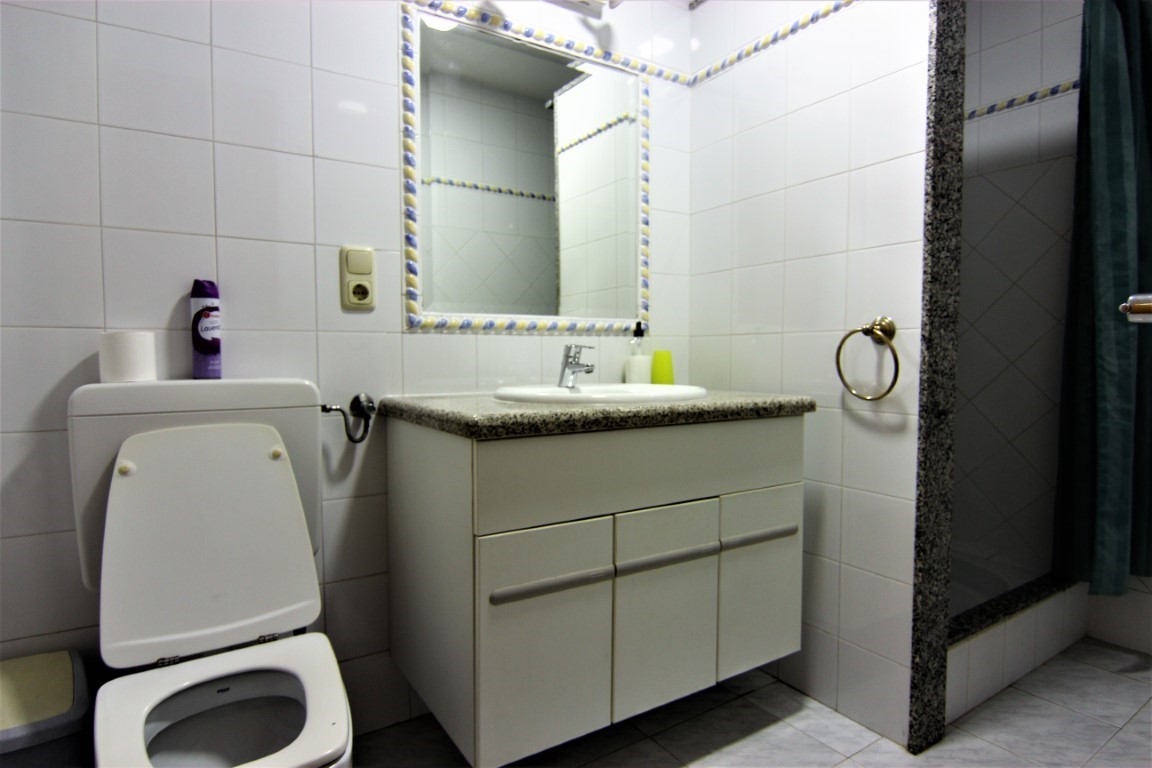 Bathroom featuring a granite countertop vanity, a decorative tiled mirror border, and a walk-in shower with natural stone trim and privacy curtain.