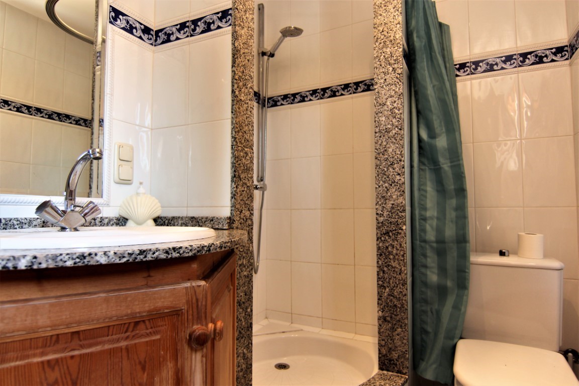 Bathroom featuring a granite countertop, wooden vanity, integrated shower with stone trim, and white wall tiles with decorative blue borders.