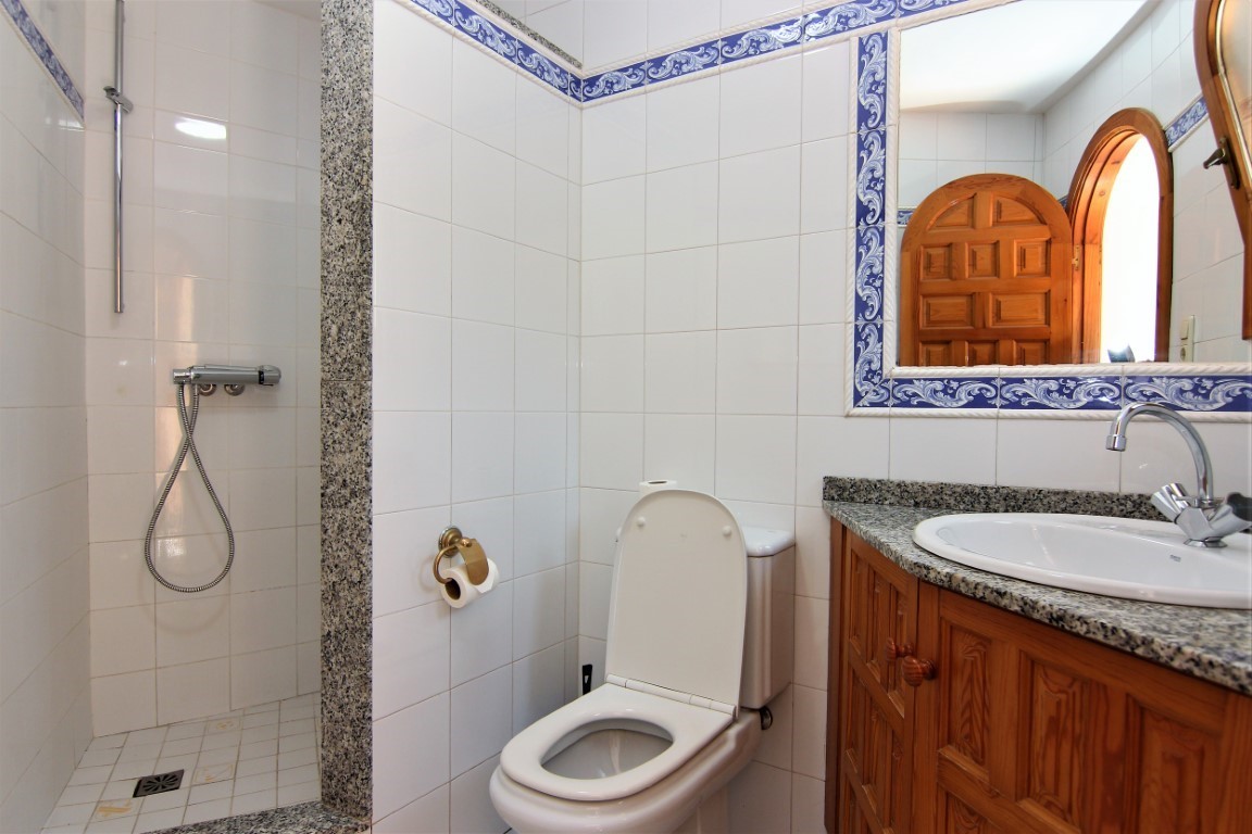 Bathroom featuring a walk-in shower with granite trim, a wooden vanity with granite countertop, and traditional blue-patterned tile borders.