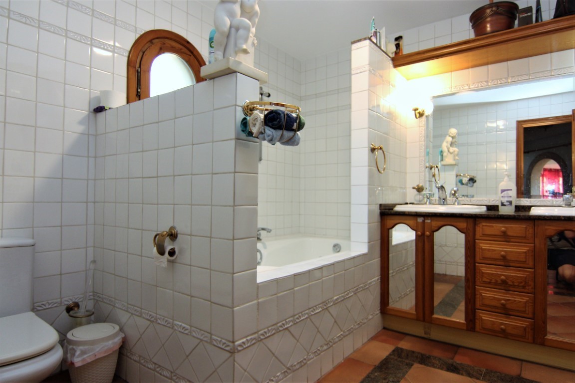 Bathroom featuring white tiled walls, a built-in bathtub, and a double wooden vanity with granite tops. Includes terracotta flooring and an arched wooden window.