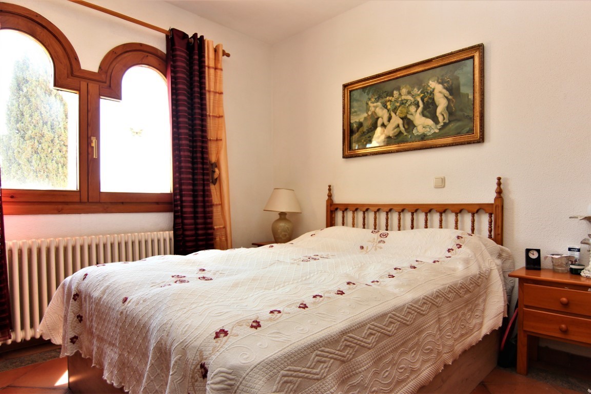 Bedroom featuring a double bed with a wooden headboard, traditional arched windows, and terracotta flooring. Natural light illuminates the classic decor.