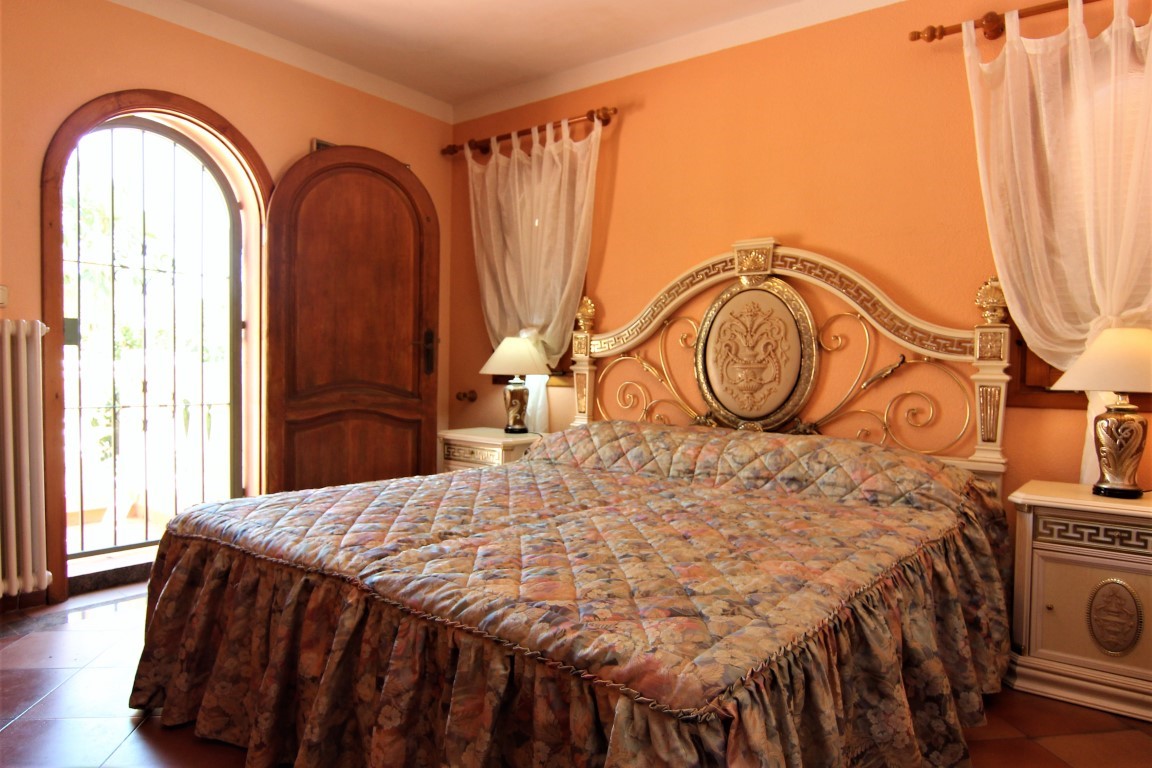 Bedroom featuring an ornate classical headboard, peach-toned walls, and an arched wooden door leading to the exterior.