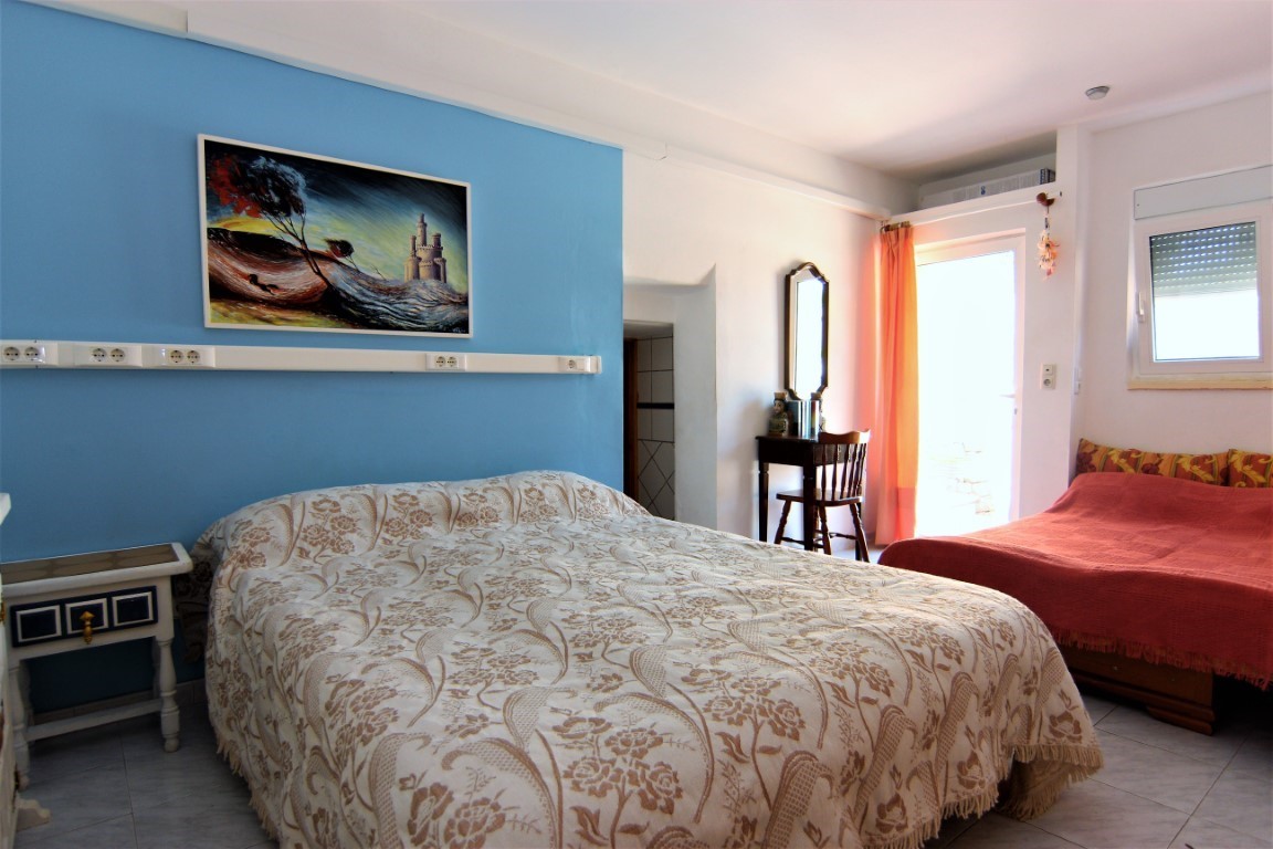 Bright bedroom featuring a blue accent wall, a double bed with floral textiles, and an additional single bed. Includes a wooden vanity, tiled flooring, and direct terrace access.