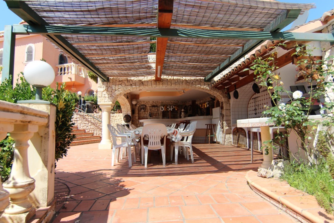 Covered terrace featuring natural stone arches, a large dining area for groups, and an outdoor kitchen under a reed-shaded pergola.