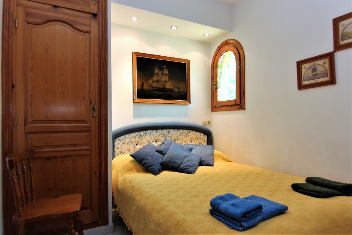 Cozy bedroom featuring a built-in wooden wardrobe, traditional arched window, and recessed spotlighting above the patterned headboard.