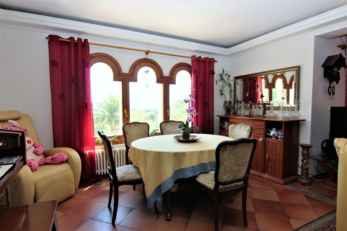 Dining area featuring a round table, upholstered chairs, and a triple arched wooden window. Includes terracotta tile flooring and a classic wooden sideboard.