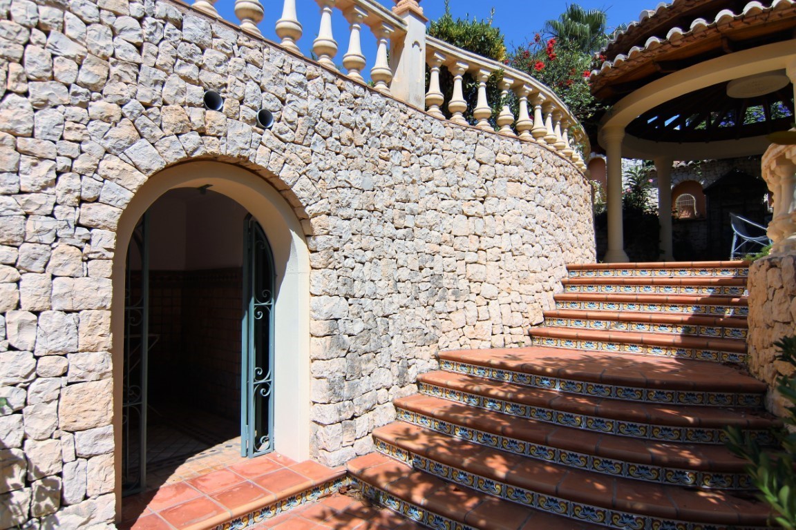 Exterior terracotta staircase featuring decorative ceramic tiles and a curved natural stone wall. Includes an arched entrance and a classic balustrade.