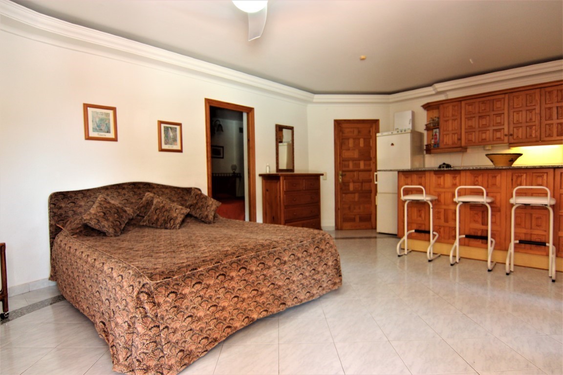 Independent studio apartment featuring a double bed, integrated wooden kitchenette with a breakfast bar, white stools, and tiled flooring.