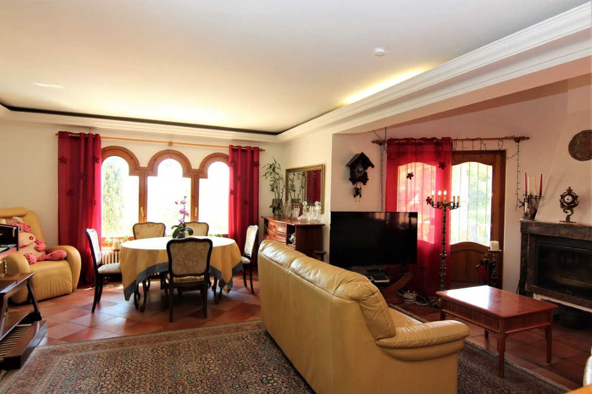 Open-plan living and dining area featuring terracotta tile flooring, a marble fireplace, and arched wooden windows. The space is illuminated by integrated cove lighting.