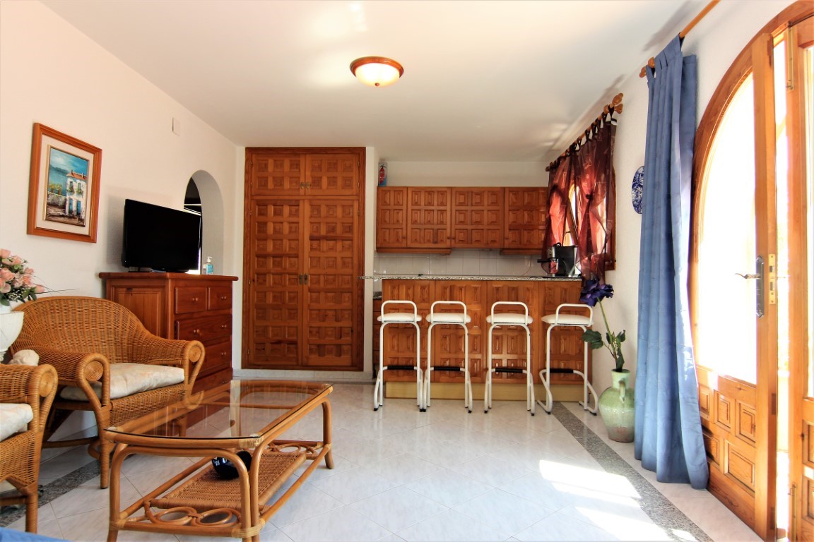 Open-plan living area featuring wicker furniture, a wooden breakfast bar with stools, and integrated cabinetry with traditional paneled doors.