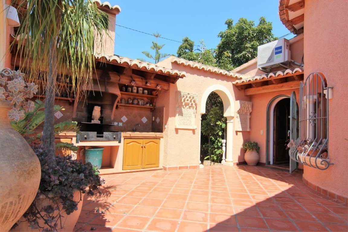 Outdoor patio featuring a covered summer kitchen with a built-in barbecue, terracotta flooring, and a decorative arched entryway in a Mediterranean style.