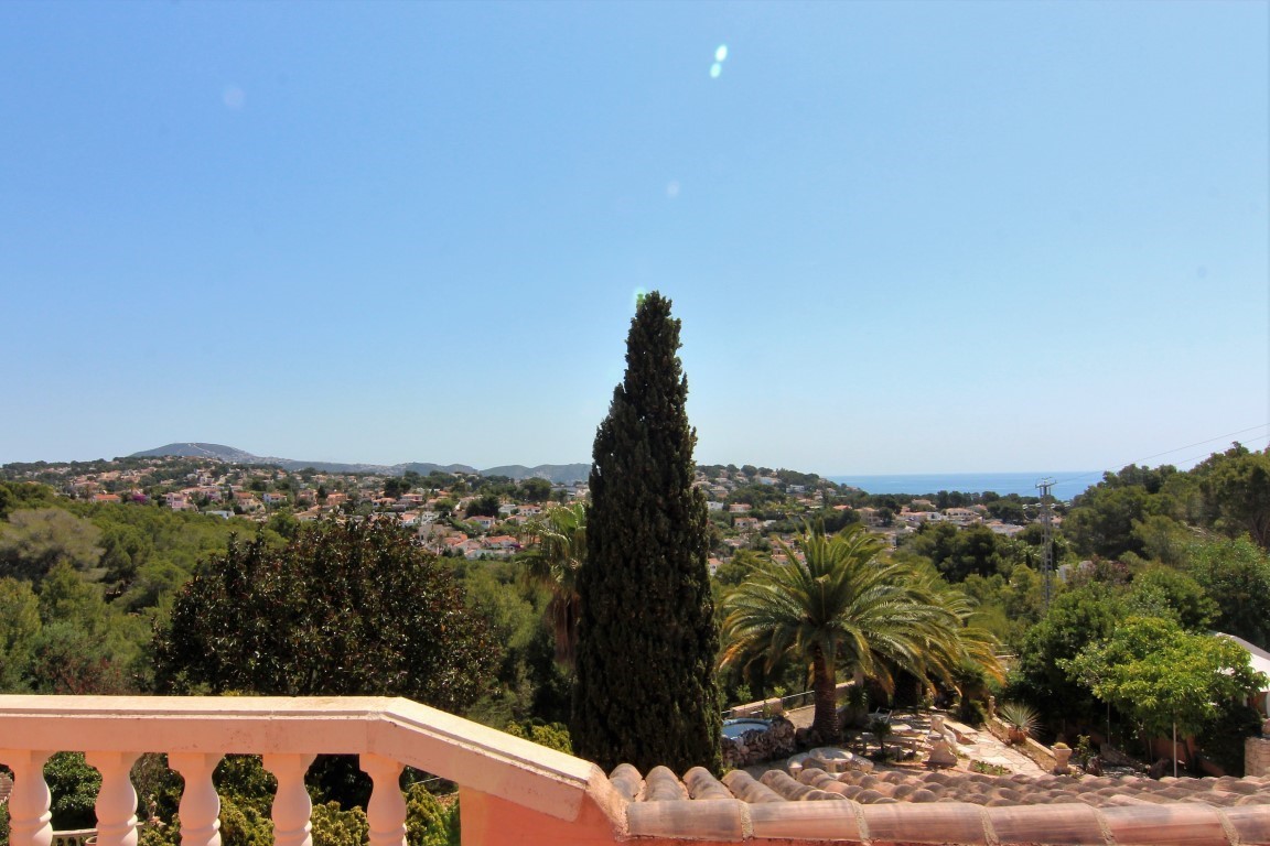 Panoramic view from the upper terrace featuring a classic balustrade, overlooking lush Mediterranean greenery, residential areas, and the sea.