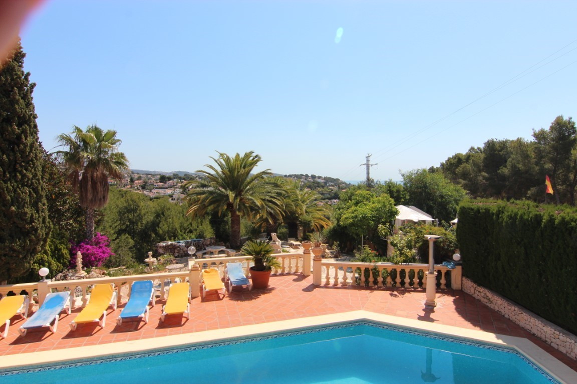 Pool terrace featuring terracotta tiling, sun loungers, and a classic stone balustrade overlooking lush Mediterranean gardens and distant sea views.