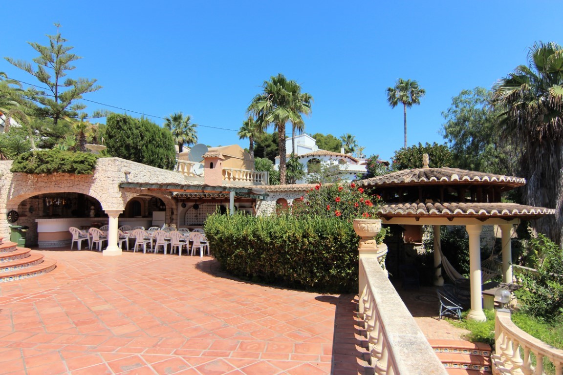 Spacious terracotta terrace featuring a stone-arched outdoor dining area and a rustic gazebo, all set within lush Mediterranean gardens with mature palm trees.