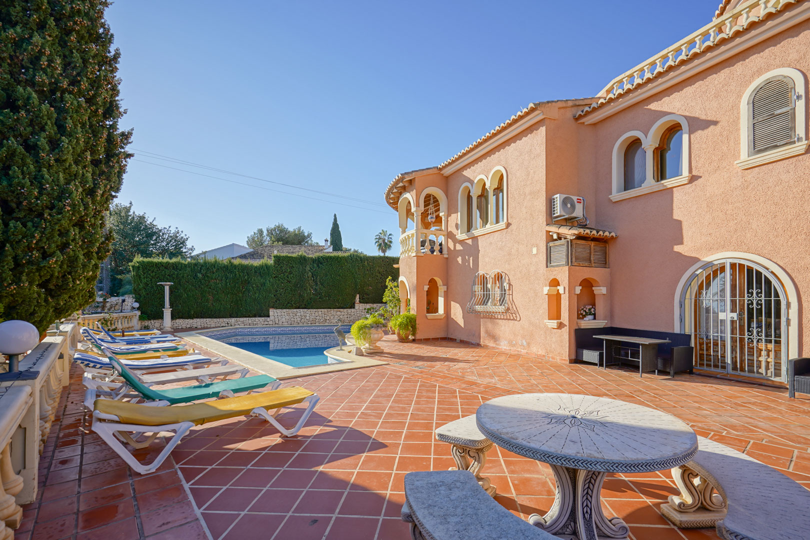 Spacious terracotta-tiled terrace featuring a private swimming pool, sun loungers, and a carved stone seating area against a Mediterranean facade.