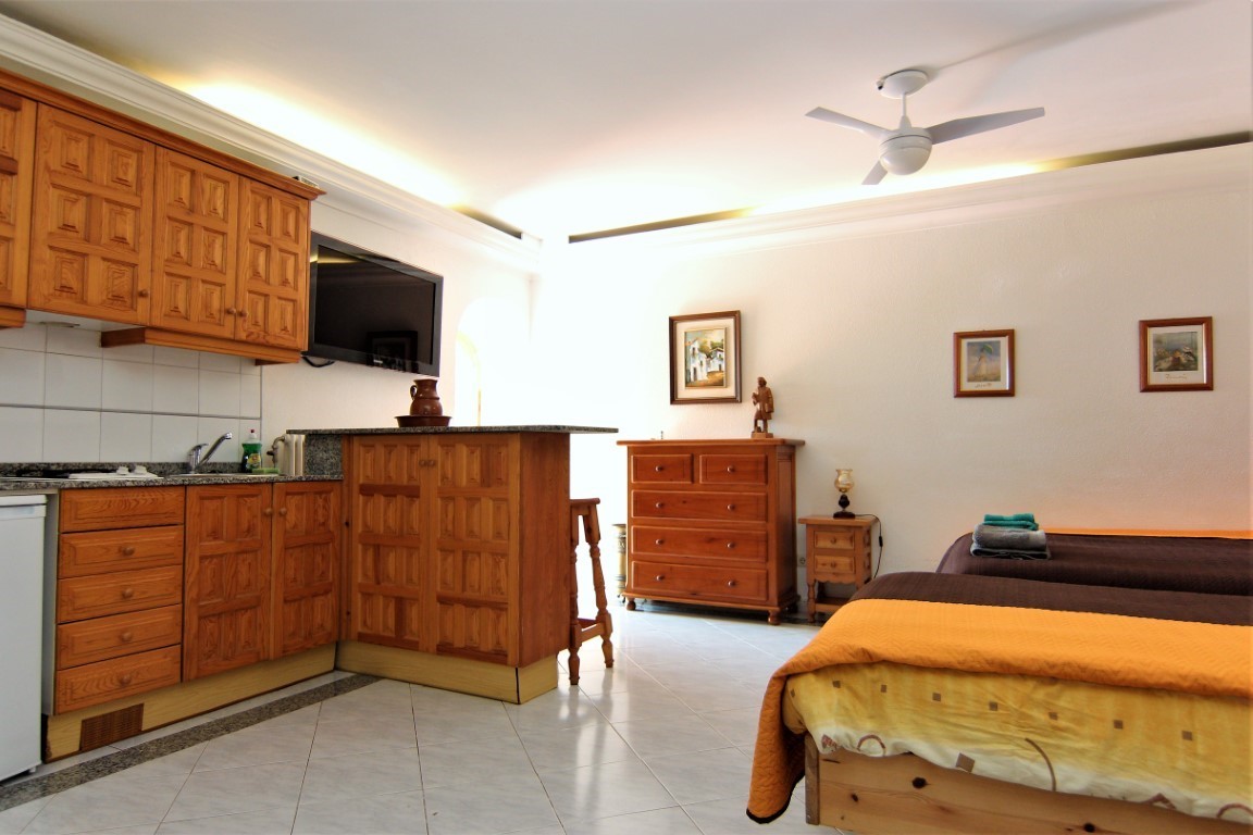 Studio suite featuring a wooden kitchenette with granite counters, twin beds, and a ceiling fan. Tiled floors and recessed lighting enhance the bright, functional layout.