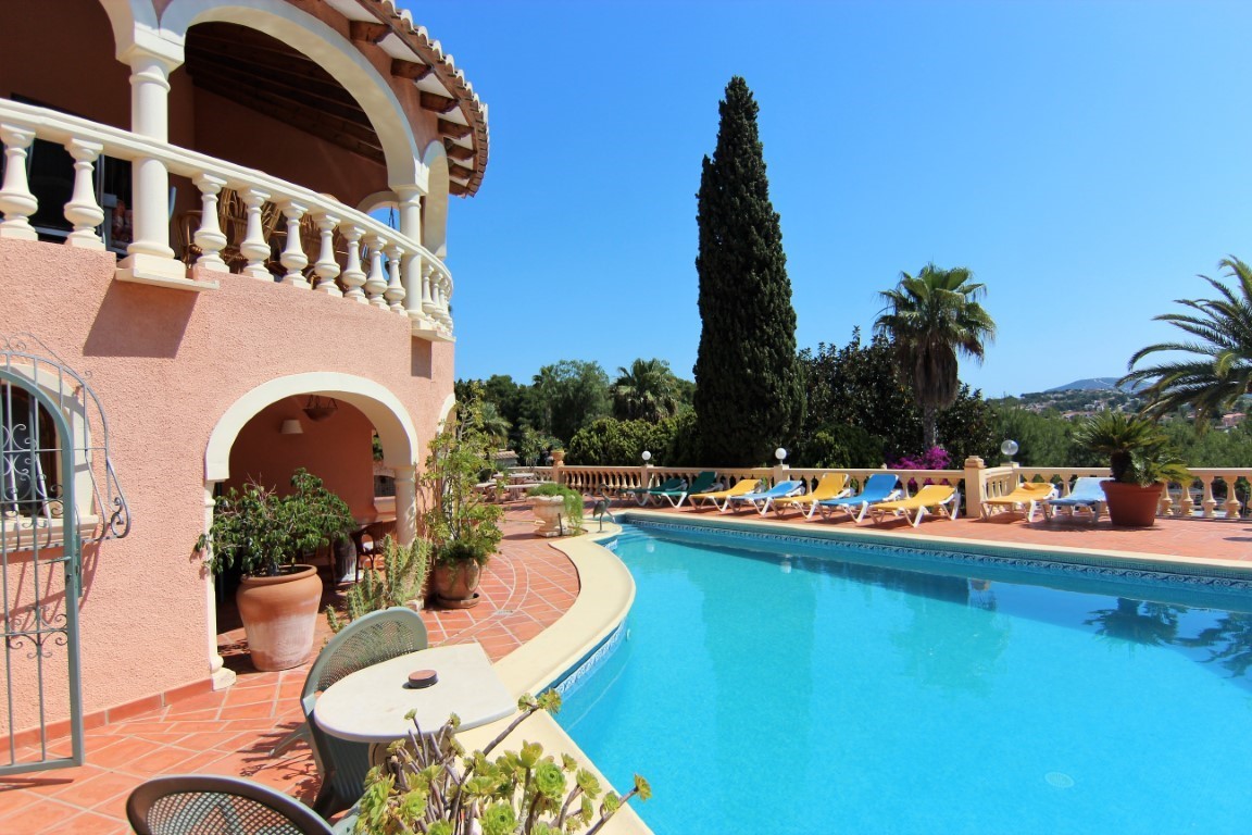 Terracotta terrace featuring a curved pool, colorful sun loungers, and a Mediterranean facade with arched balconies and white stone balustrades.