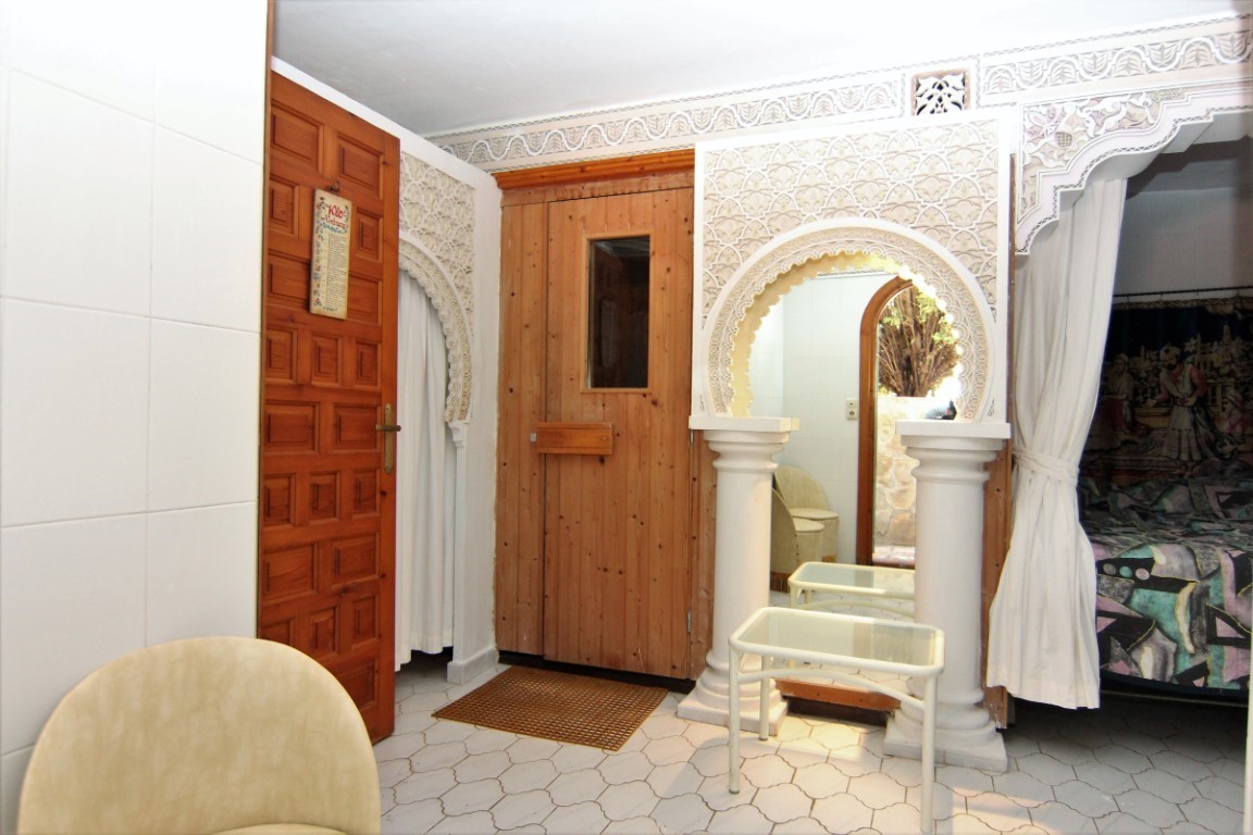 Wellness area featuring a wooden sauna, intricate Moorish-style plaster arches with columns, and white hexagonal floor tiles.