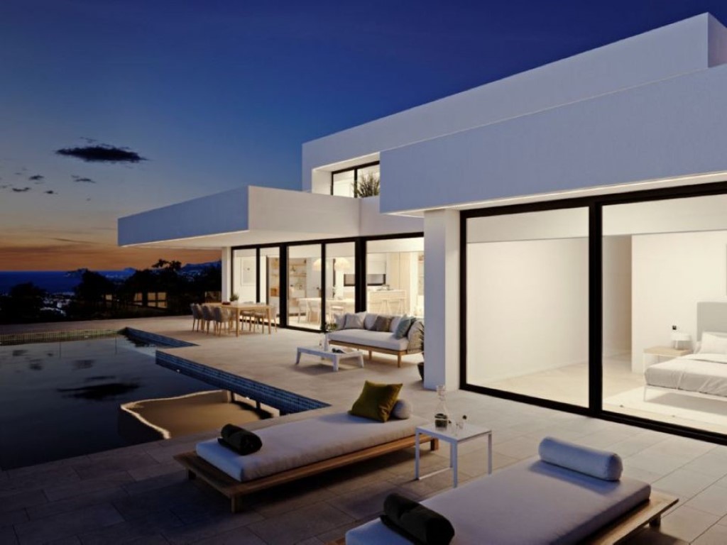Modern villa exterior at dusk featuring floor-to-ceiling glass walls, a spacious stone terrace with infinity pool, and coastal views.