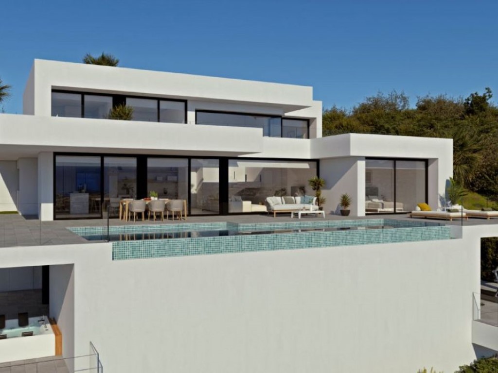 Modern white villa exterior featuring an infinity pool with turquoise tiles, expansive terraces, and floor-to-ceiling glass doors connecting indoor and outdoor living.
